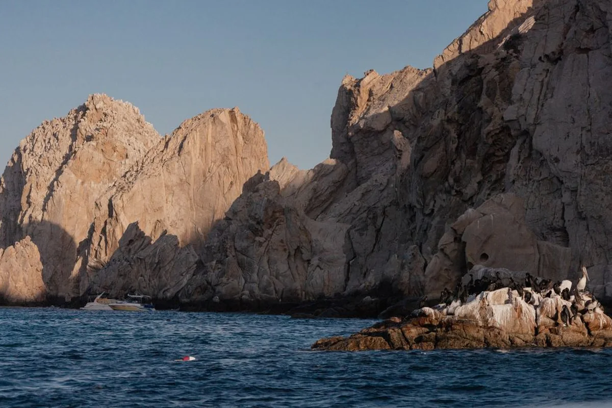 The granite cliffs of Land's End at Cabo San Lucas, with a small boat anchored below and seabirds on the rocks